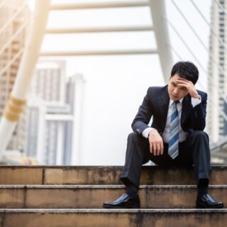 رجل بالغ يرتدي بدلة رسمية ويجلس على الدرج في أحد الشوارع ويضع يد على جبينه وهو يظهر حزينا