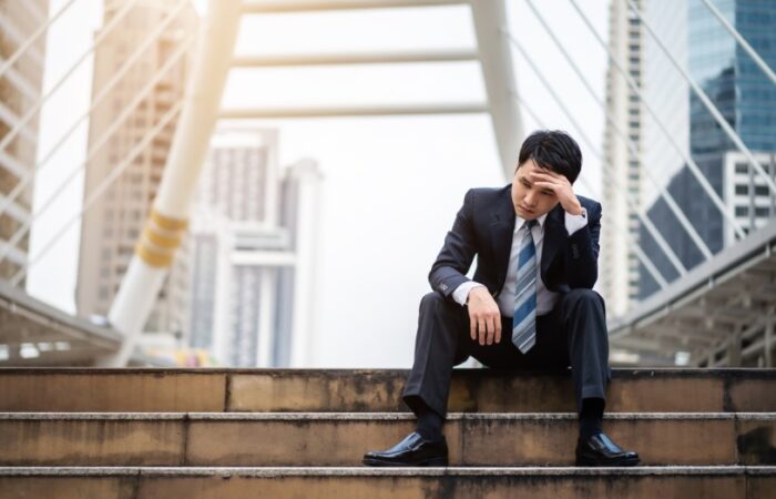 رجل بالغ يرتدي بدلة رسمية ويجلس على الدرج في أحد الشوارع ويضع يد على جبينه وهو يظهر حزينا