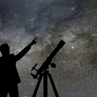 رجل يشير للسماء بيده وبجانبه جهاز تلسكوب