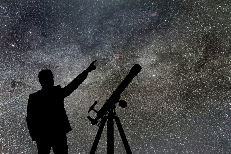 رجل يشير للسماء بيده وبجانبه جهاز تلسكوب