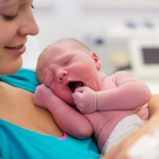 امرأة ترتدي كنزة زرقاء وتحمل بيدها طفل رضيع يشعر بالنعاس