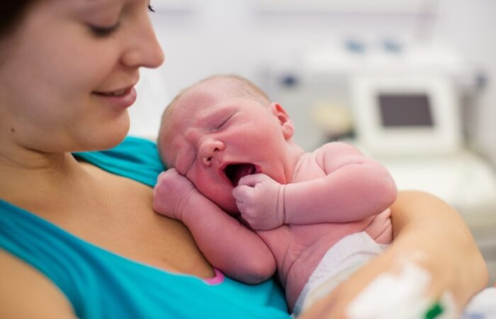 امرأة ترتدي كنزة زرقاء وتحمل بيدها طفل رضيع يشعر بالنعاس