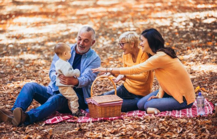 امرأة كبيرة بالسن وامرأة صغيرة بالسن ورجل كبير بالعمر يحمل طفل يجلسون بالحديقة على الأرض
