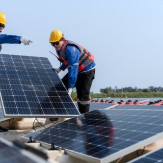 رجلان يقفان على سطح منزل ويمسكان بلوح الطاقة الشمسية مستطيلة الشكل