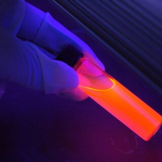 شخص يُمسك بعلبة اسطوانية شفافة فيها سائل برتقالي وُمحاطة باللون الأزرق