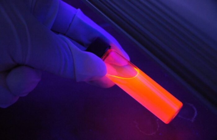 شخص يُمسك بعلبة اسطوانية شفافة فيها سائل برتقالي وُمحاطة باللون الأزرق