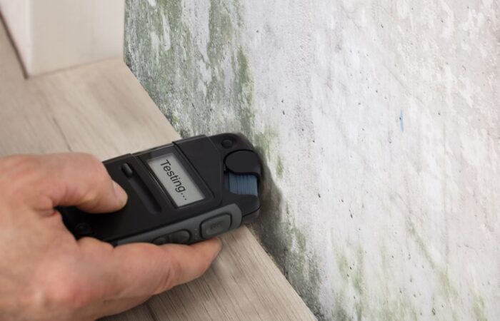 شخص يقوم بوضع جهاز قياس سماكة البيتون على جدار مسلح ومكتوب على الجهاز كلمة جاري الاختبار باللغة الانكليزية