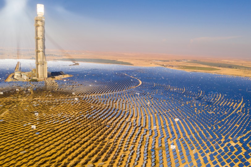 مجموعة من الألواح العاكسة لأشعة الشمس موزعة بشك دائري كبير يعكس الضوء نحو قمة برج معدني موجود في منتصف هذا الحقل
