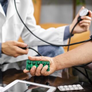 طبيب يقيس ضغط الدم لشخص يحمل ظرف دواء أخضر في يده