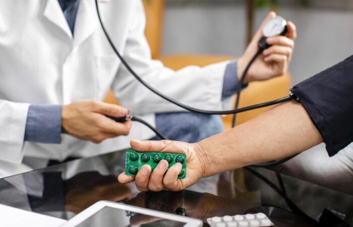 طبيب يقيس ضغط الدم لشخص يحمل ظرف دواء أخضر في يده