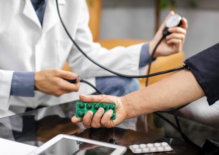 طبيب يقيس ضغط الدم لشخص يحمل ظرف دواء أخضر في يده