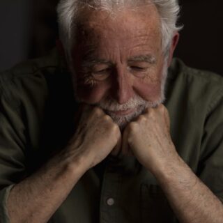 رجل مسن شعره أبيض يجلس حزينا ويضع يديه على ذقنه