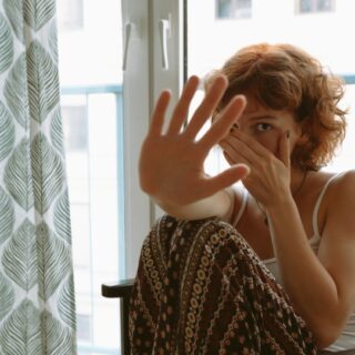 امرأة شعرها قصير بني اللون تجلس على كرسي قرب نافذة وتضع إحدى يديها على وجهها