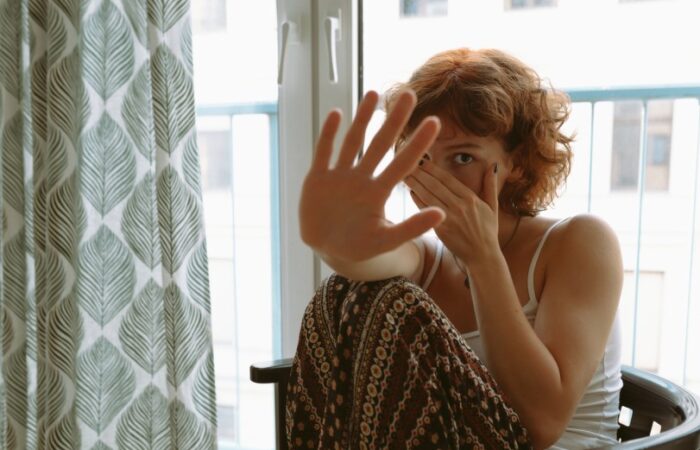 امرأة شعرها قصير بني اللون تجلس على كرسي قرب نافذة وتضع إحدى يديها على وجهها