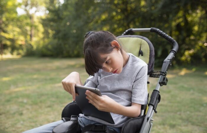 فتاة صغيرة تجلس على كرسي متحرك في الحديقة ورأسها منحني للأسفل