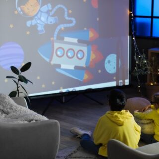 ولد وبنت يرتدون جاكيت صفراء اللون يجلسون على الأرض ويشاهدون أفلام كرتون على شاشة تلفاز ضخمة