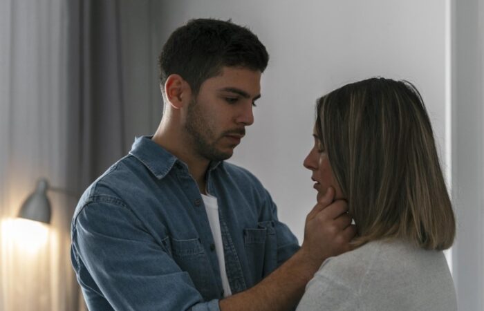 رجل يرتدي قميص أزرق وينظر لا مرأة مغمضة العينين ويضع يده على خدها