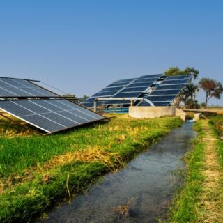 مجموعة من ألواح الطاقة الشمسية المتواجدة في حقل زراعي وبجانبها انبوب معدني تخرج منه المياه