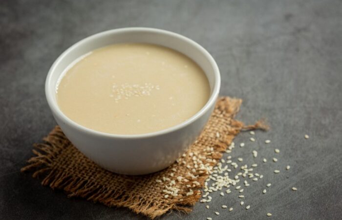 سائل بني اللون مائل للون الأبيض ضمن كأس زجاجي أبيض اللون وبجانب الكأس بذور صغيرة بيضاء اللون