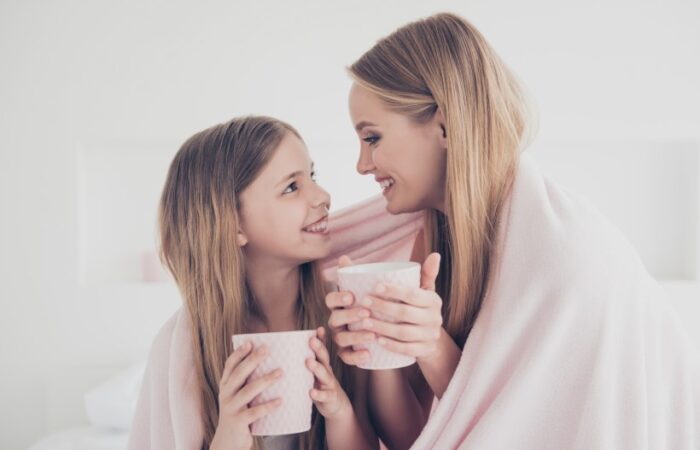 امرأة مبتسمة تمسك كوب بيدها وتنظر لفتاة تجلس بجانبها ويضعون غطاء على أكتافهم