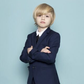 صبيّ صغير شعره أشقر اللون ويرتدي بدلة رسمية يقف مكتوف الأيدي