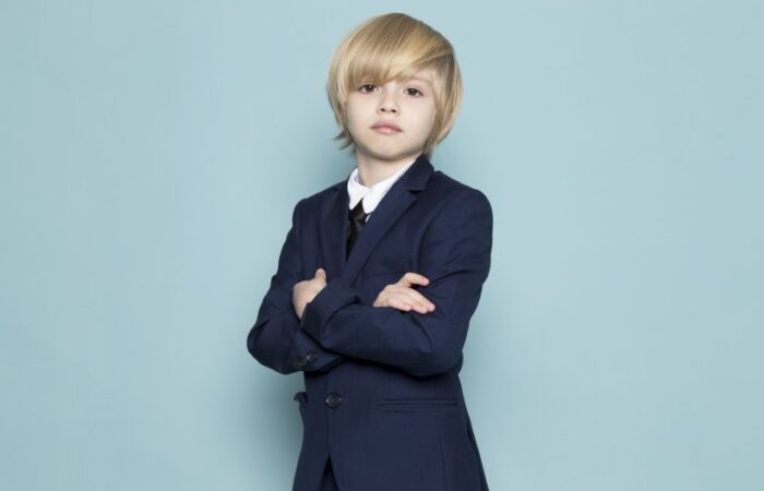 صبيّ صغير شعره أشقر اللون ويرتدي بدلة رسمية يقف مكتوف الأيدي