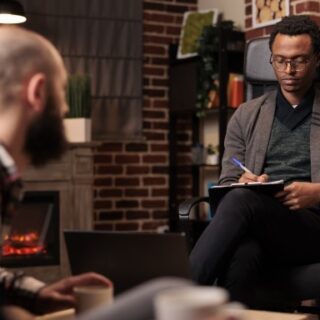 رجل يجلس على كرسي ويمسك قلم ودفتر ورجل آخر يجلس بمواجهته