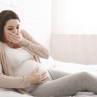 امرأة حامل مستلقية على السرير تضع يدها على فمها واليد الأخرى على بطنها