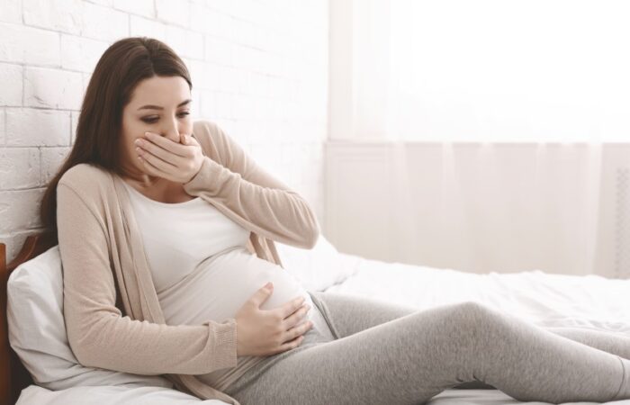 امرأة حامل مستلقية على السرير تضع يدها على فمها واليد الأخرى على بطنها
