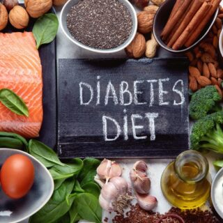 لوحة سوداء مكتوب عليها بالإنكليزية Diabetes diet وحولها خضار متنوعة كالبروكلي والسبانخ بالإضافة للبيض والسمك وزيت الزيتون ومكسرات كاللوز والجوز