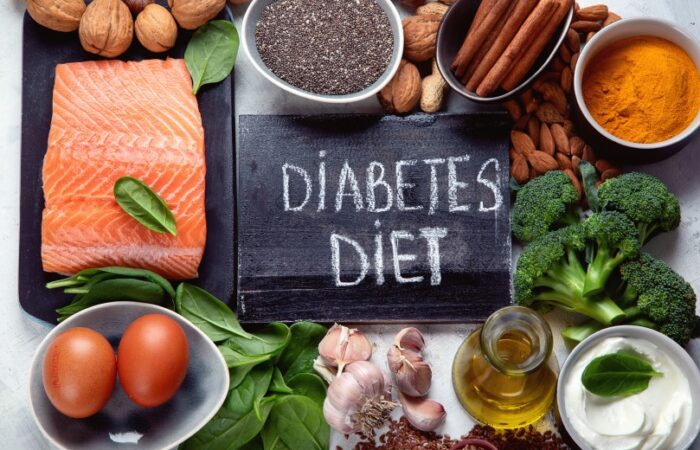 لوحة سوداء مكتوب عليها بالإنكليزية Diabetes diet وحولها خضار متنوعة كالبروكلي والسبانخ بالإضافة للبيض والسمك وزيت الزيتون ومكسرات كاللوز والجوز