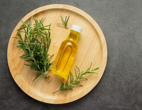 زجاجة صغيرة تحتوي سائل أصفر اللون وبجانبها عود إكليل الجبل الأخضر