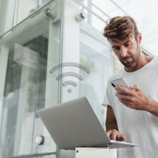 رجل يحمل بيده هاتف محمول وبيده الأخرى يعمل على اللابتوب مستخدما شبكة واي فاي