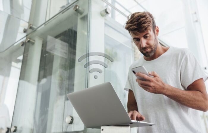 رجل يحمل بيده هاتف محمول وبيده الأخرى يعمل على اللابتوب مستخدما شبكة واي فاي