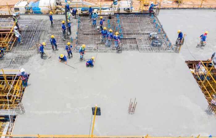 العديد من عمّال البناء يقومون بصب سقف مبنى وتقف بجانب المبنى آليات نقل الخرسانة