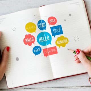 يد فتاة تمسك بقلم وتشير لدفتر مرسوم عليه دوائر ملونه وكل دائرة مكتوب بداخلها كلمة بلغة معينة