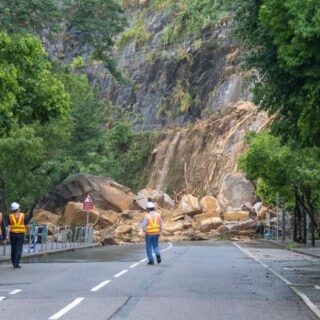 طريق جبلي مسدود بصخور كبيرة منهارة من جانب الطريق وثلاثة عمال طرق يقومون بمعاينة الموقع