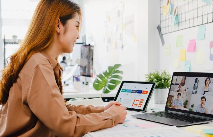 امرأة مبتسمة تنظر لشاشة اللابتوب وتتحدث مع أشخاص وبجانبها أيباد مرسوم على شاشته جدول بيانات