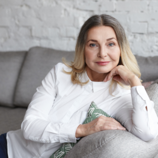 امرأة أربعينية مبتسمة تجلس على الأريكة وتضع يدها على خدها