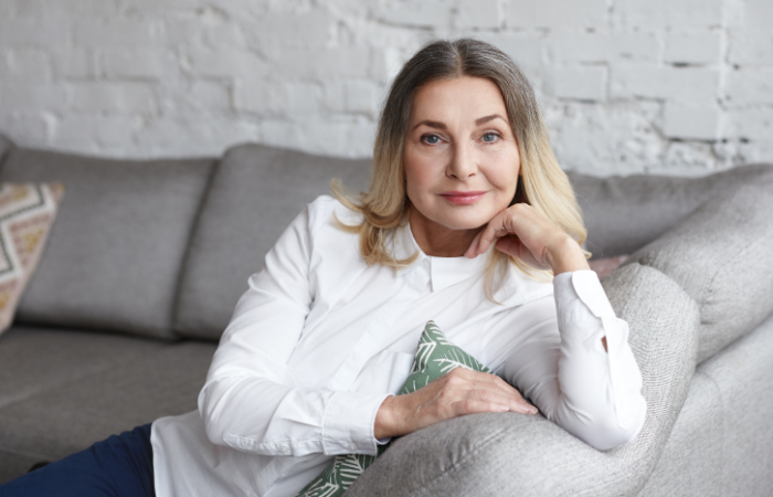 امرأة أربعينية مبتسمة تجلس على الأريكة وتضع يدها على خدها