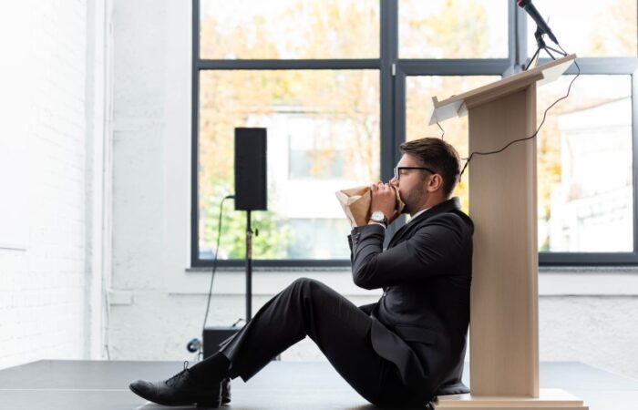 منظر جانبي لرجل أعمال خائف يرتدي بدلة ويتنفس في كيس ورقي أثناء المؤتمر