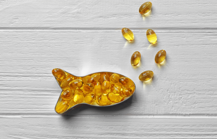 كبسولات من زيت كبد سمك القد مرتبة على شكل سمكة على خلفية خشبية بيضاء