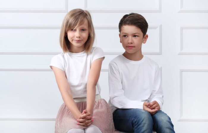 بنت ترتدي تنورة زهرية اللون وكنزة بيضاء تجلس بجانب صبي يرتدي كنزة بيضاء اللون وبنطال جينز