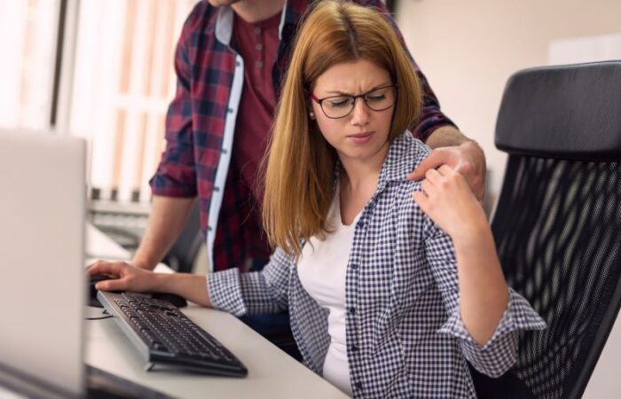 رجل يضع يده على كتف امرأة وهي جالسة أمام طاولة الكمبيوتر