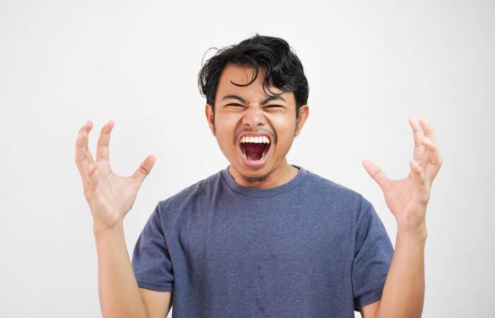 شاب أسيوي يرتدي كنزة زرقاء اللون يصرخ بجنون وهو يرفع يديه