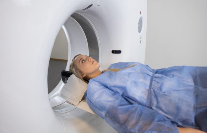 مريضة تلبس لباس أزرق اللون وتستلقي على سرير جهاز طبي دائري الشكل ويتم إدخالها اليه