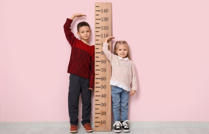 بنت وصبي يضعان أيديهم أعلى رأسهم ويقفان على جانبي مقياس الطول الموجود على الحائط