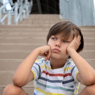 طفل حزين يجلس على الدرج ويضع يدّ على خده