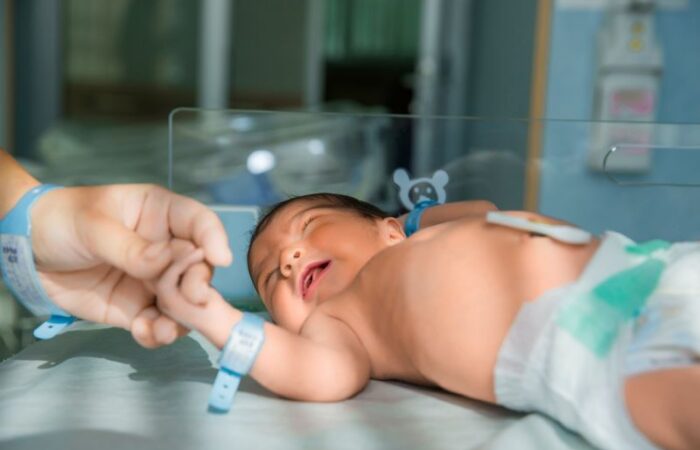 يد شخص تمسك بيد طفل رضيع مستلقي في حاضنة الأطفال في المستشفى