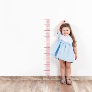فتاة صغيرة تقف بجانب مقياس الطول المرسوم على الحائط وتضع يدها فوق رأسها
